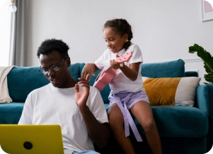 Father and daughter look at laptop by couch